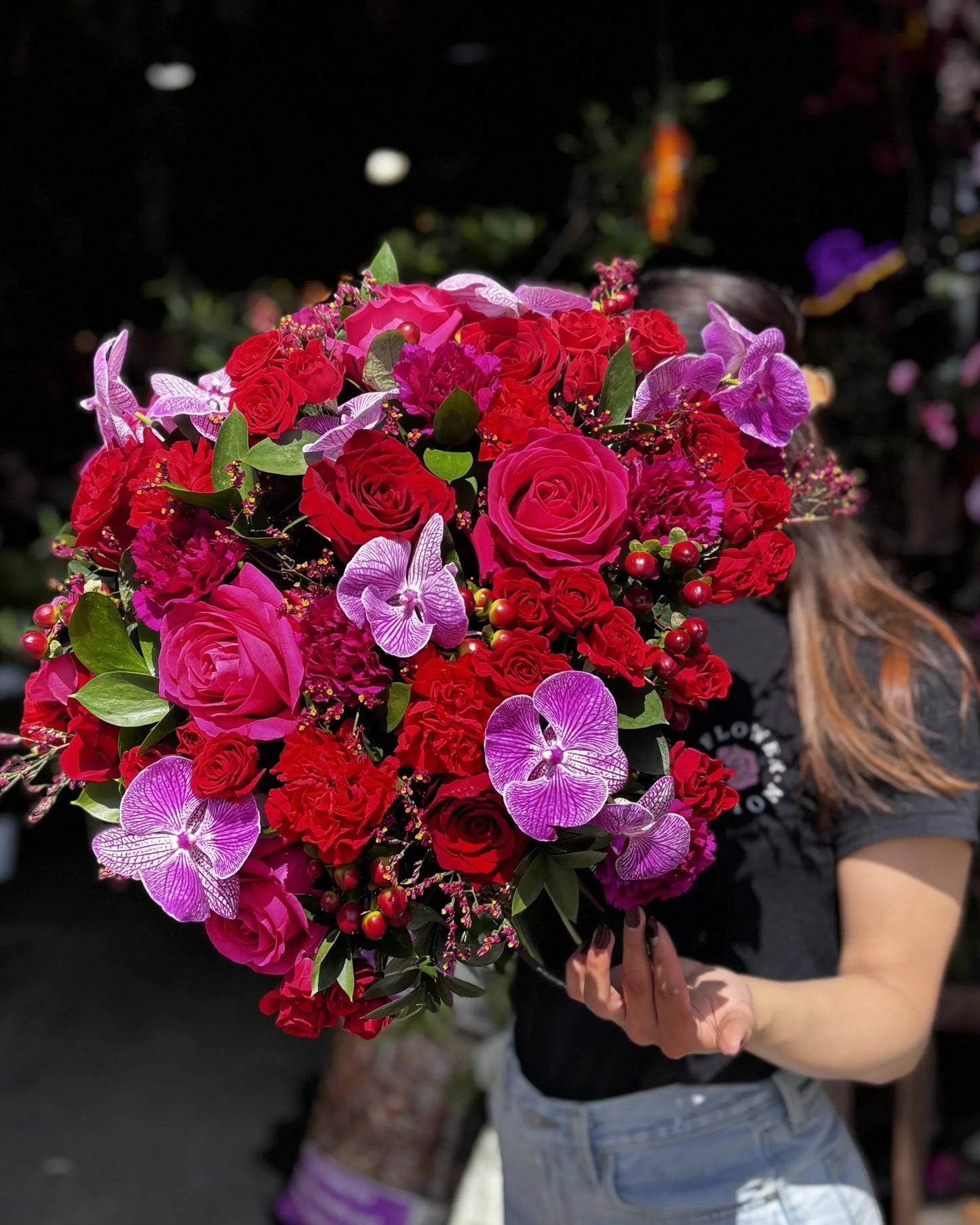 Flower Station Avenue Q bouquet featuring red Ecuadorian roses, purple vanda orchids, and dahlias held by a person.